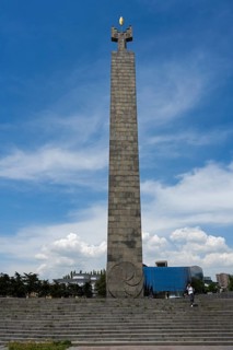 Tall stone column with symbolically decorated top under blue sky, memorial to 50 years of Soviet