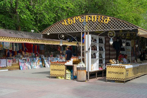 Market square with stalls selling books and souvenirs under a wooden frame outdoors, Vernissage
