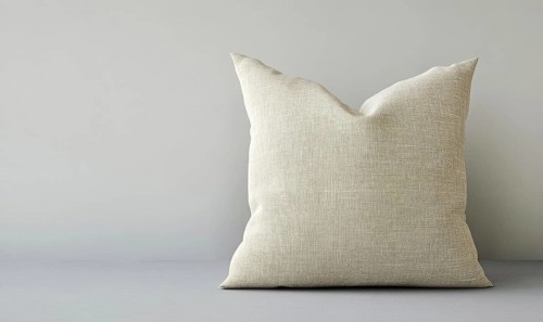 A white pillow with a pattern on it sits on a grey surface. The pillow is large and fluffy, and it