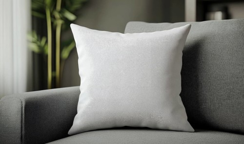 A white pillow sits on a gray couch. The pillow is the main focus of the image, and it is a