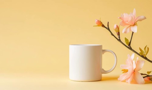 A white coffee cup sits on a yellow background with pink flowers in the foreground. Concept of calm