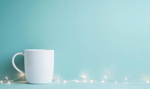 A white coffee cup sits on a blue background. The cup is the main focus of the image, and the blue