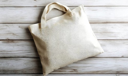 A white bag with a handle sits on a wooden surface. The bag is empty and has a simple design.