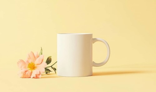 A white coffee cup with a flower on top of it. The flower is pink and the cup is empty. AI