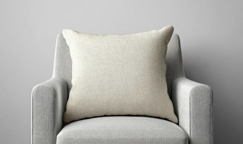 A white pillow on a gray chair. The pillow is large and has a textured surface. The chair is also