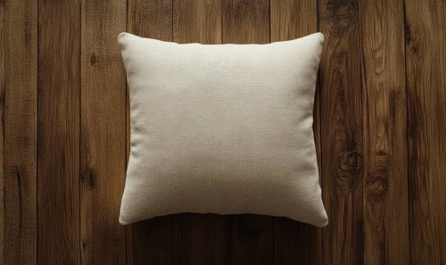 A white pillow sits on a wooden surface. The pillow is unmade and has a simple design. The wooden