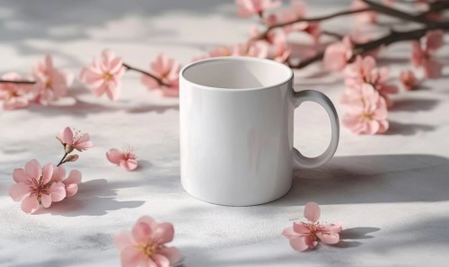 A white coffee cup sits on a table with pink flowers in the background. The cup is empty and the