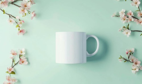 A white coffee cup sits on a green background with pink flowers. The cup is empty and the flowers