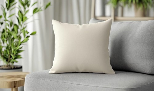 A white pillow sits on a gray couch in a living room. The pillow is placed on a chair and is