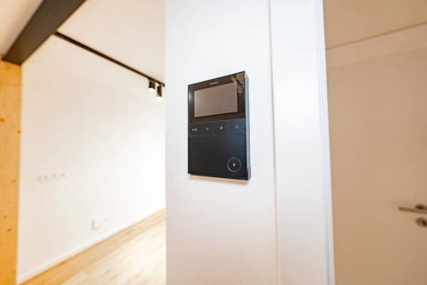 Wall intercom with display in a bright corridor next to a white door and warm parquet, house