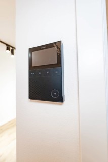 Black video intercom system with display on white wall in modern entrance area, house renovation,