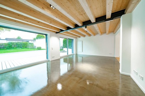 Open living room with wooden beam ceiling and polished concrete floor, flooded with light through