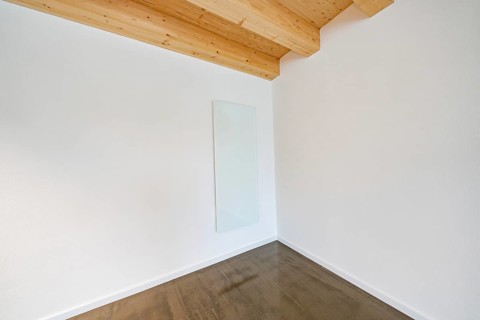 Bright corner with glass heating panel on white wall under wooden beam ceiling, reduced appearance,