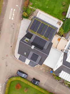 Top view of house with PV modules and carport green roof, two parked cars and curved road, house