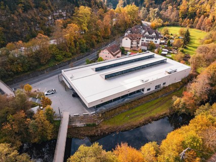 Sports hall nestled in an autumnal setting with a small river and bridge nearby, Walter Lindner