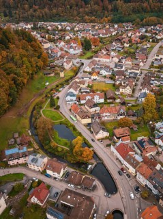 Aerial view of a city with river course and park area, nestled in autumn surroundings, Calmbach,