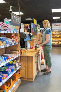 A woman sticks a brown shopping bag near the cash register, surrounded by products, 24 hours Aunt M