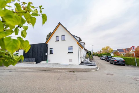 Side view of a bright residential building in a quiet settlement with parked cars and hedges, house
