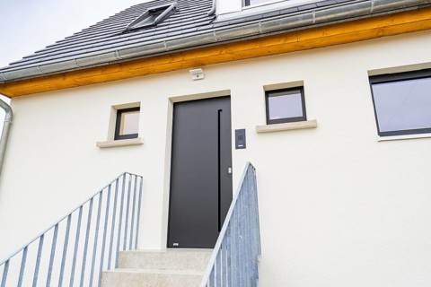 Modern house entrance with dark grey door and simple windows, staircase with metal railing, quiet