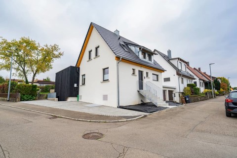 Modernized residential building on a quiet street corner with bright façade under cloudy sky, house