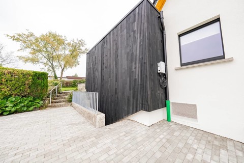 Modern house side with black wood paneling on paved driveway, house renovation, air conditioning