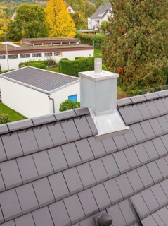 Fireplace with metal cladding on anthracite-colored roof, view over the residential area, house