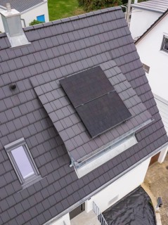 Detail of the roof opening with glass balustrade and two solar modules next to a skylight on a