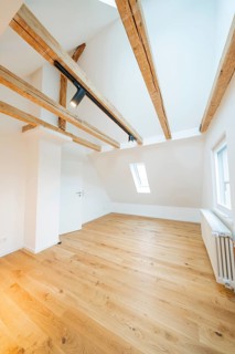 Light-flooded room under the roof with warm wooden floors and visible beam ceiling, house