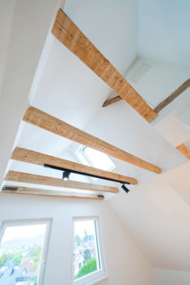 View of ceiling beams with skylight and rail spot in a bright attic room, house renovation, climate