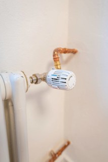 Detail of a radiator thermostat with copper lines on a white wall, house renovation, climate