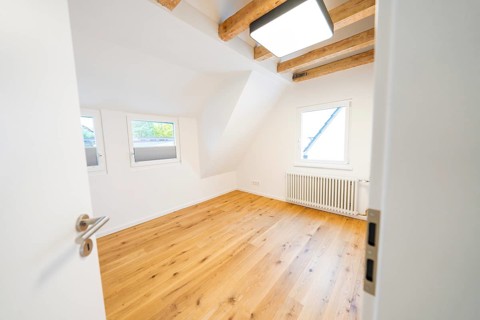Light-flooded attic room with oak floors and visible beams, freshly renovated and minimalistic