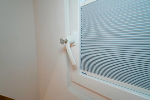 Detail of a lockable white window handle with integrated blind, house renovation, climate