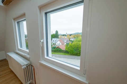 Bright room with white windows and views of residential buildings and greenery, radiator on the