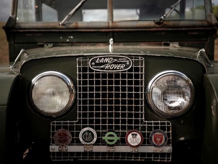 The front end of a 1950's Series One Land Rover, adorned with hunt club badges on the front grill,