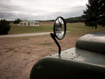 A cracked review mirror reflects a hood ornament on a 1950's Series One Land Rover on August 8,