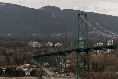 A long suspension bridge connecting a cityscape with mountainous surroundings under an overcast sky