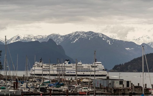 Ferry docked at a harbor with mountain range and snow in the background on a cloudy day in