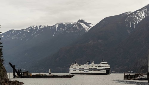 A ferry cruises through a scenic region with snowy mountains and cloudy skies in Horseshoe Bay,