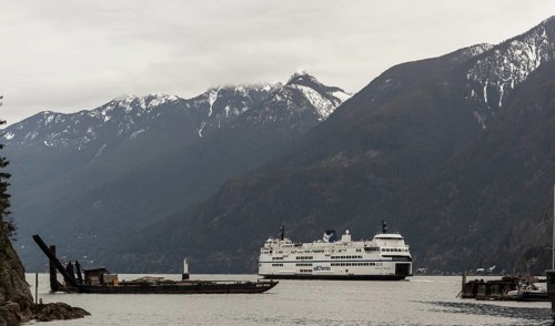 A ferry sails through calm waters with snow-capped mountains in the background in Horseshoe Bay,