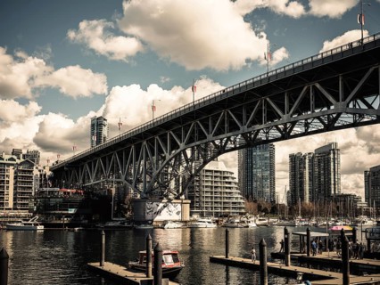 A grand bridge stretches over a busy harbor against a backdrop of clouds in Vancouver, British