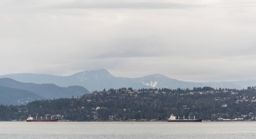 Distant view of ships passing by mountain-lined shores under cloudy skies in Vancouver, British