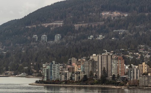 Urban high-rise buildings set against a backdrop of forest and mountains on an overcast day in