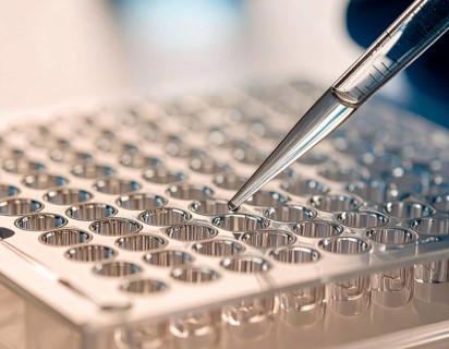 Clear pipette delivers a droplet to a transparent microplate under warm lab light, Pipette