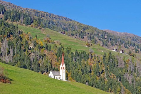 Lonely church with red tower on green alpine slope under bright blue sky, Dolomites, Drau cycle