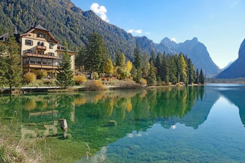 Waterfront villa on a clear mountain lake reflected against rugged peaks, sunny autumn colors glow