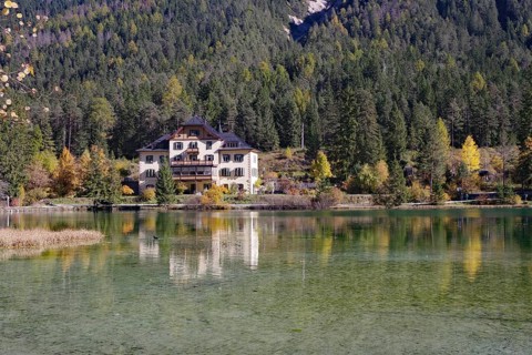 The villa is brilliantly reflected in a quiet alpine lake in front of dense forest and gentle