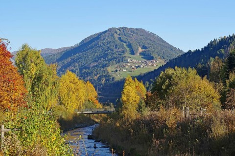 A stream snakes through an autumnal valley, on the sunny mountainside there is a village under deep