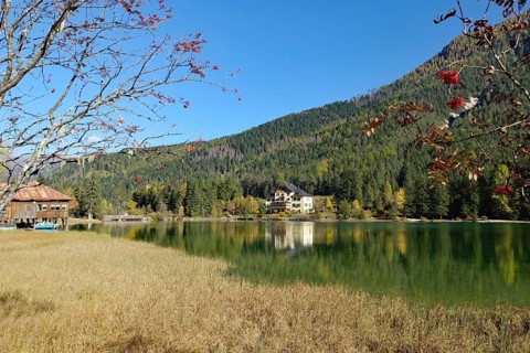 Autumnal alpine lake with clear water, a lakeside hut and red berry branches frame the view of the