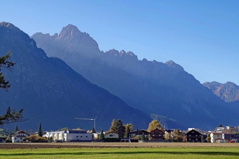 Village at the foot of rugged mountains, wide meadow in the foreground, clear air and soft light,