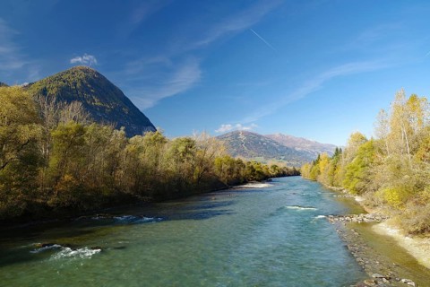 Wide river snakes through an autumnal valley, quiet sky with fine contrails, Lienz, Drau cycle